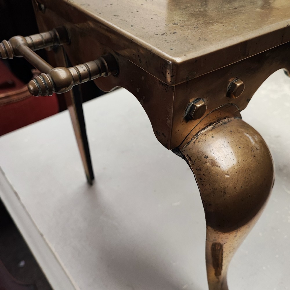 A Georgian brass hearth footman featuring a smooth rectangular top, side drop handles, a scalloped apron, and front cabriole legs with paw feet. View V
