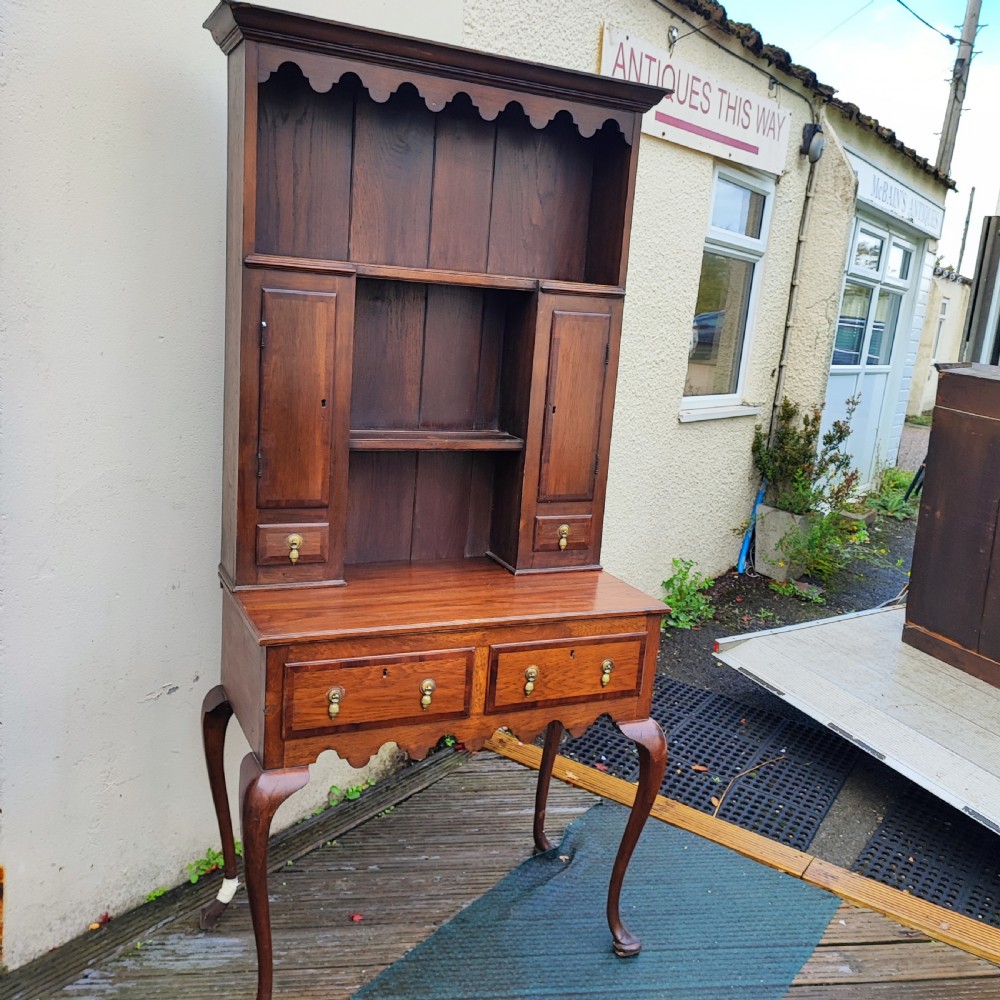 An antique dark oak small dresser featuring an open shelving unit with side cupboards over a two-drawer base raised on cabriole legs.
