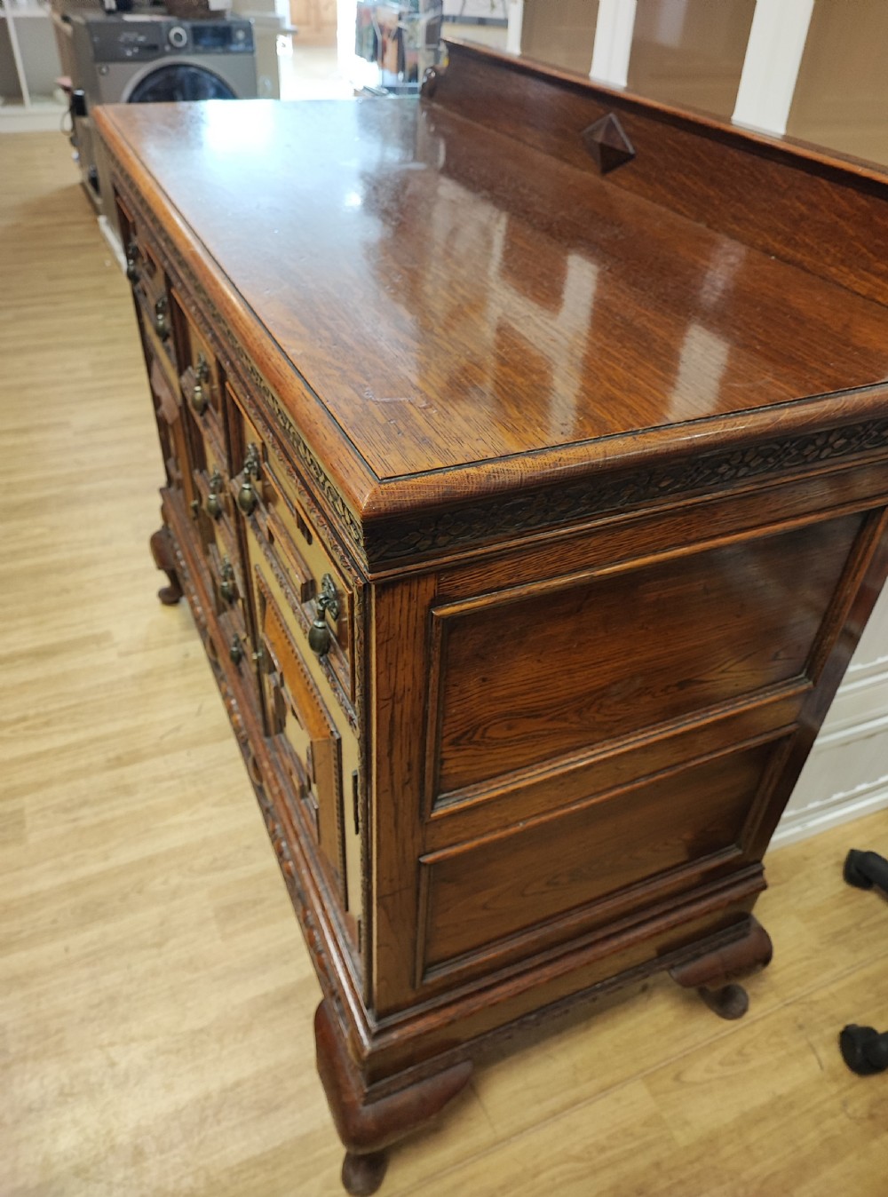 A carved dark oak sideboard featuring geometric panelled cupboard doors, multiple drawers with brass drop handles, cabriole legs, and a low upstand. View III