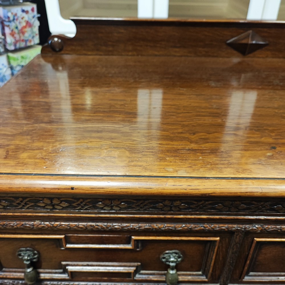 A carved dark oak sideboard featuring geometric panelled cupboard doors, multiple drawers with brass drop handles, cabriole legs, and a low upstand. View V