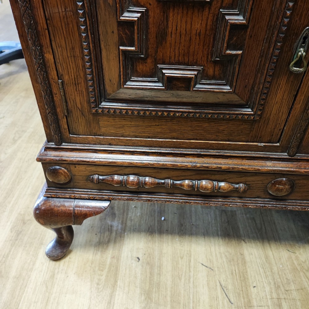 A carved dark oak sideboard featuring geometric panelled cupboard doors, multiple drawers with brass drop handles, cabriole legs, and a low upstand. View IX