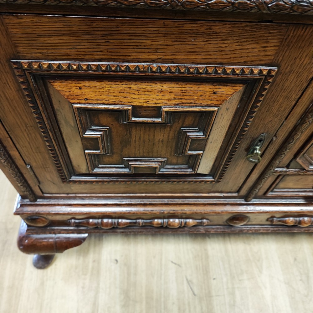 A carved dark oak sideboard featuring geometric panelled cupboard doors, multiple drawers with brass drop handles, cabriole legs, and a low upstand. View X