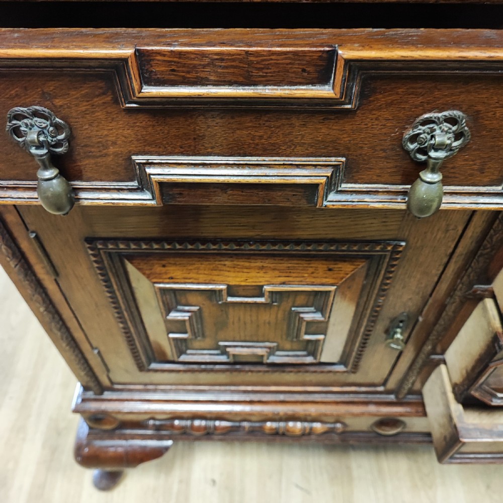 A carved dark oak sideboard featuring geometric panelled cupboard doors, multiple drawers with brass drop handles, cabriole legs, and a low upstand. View XII