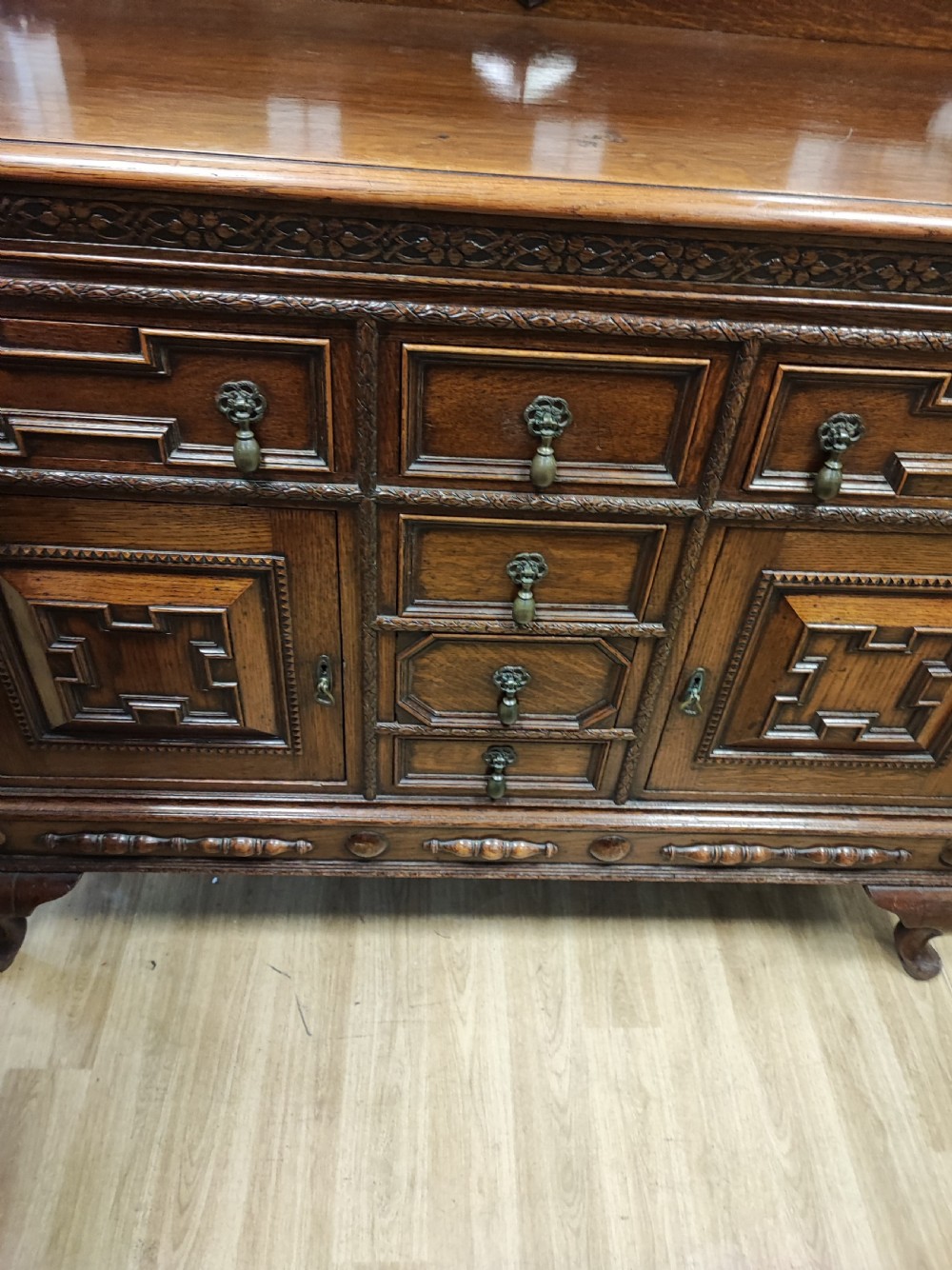 A carved dark oak sideboard featuring geometric panelled cupboard doors, multiple drawers with brass drop handles, cabriole legs, and a low upstand. View XIII
