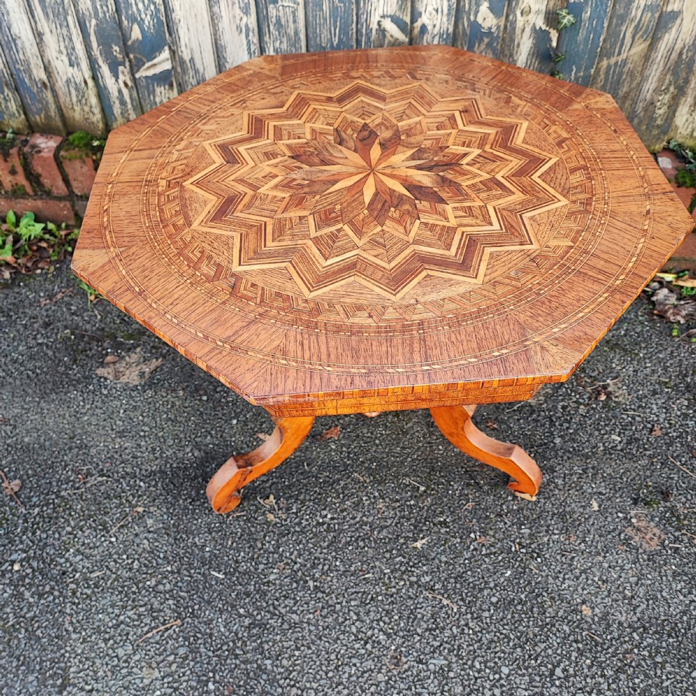 An octagonal wood low table featuring an intricate geometric starburst marquetry pattern on top, set on curved legs.