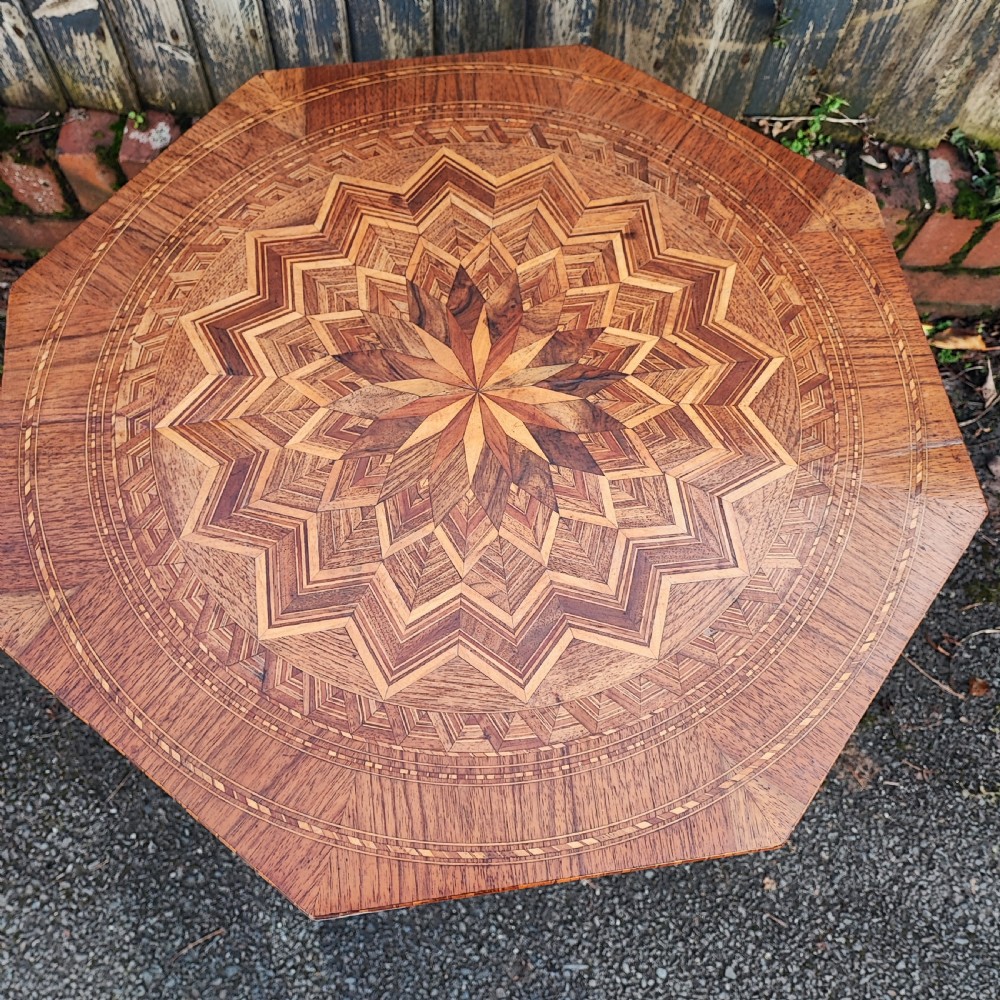 An octagonal wood low table featuring an intricate geometric starburst marquetry pattern on top, set on curved legs. View IV