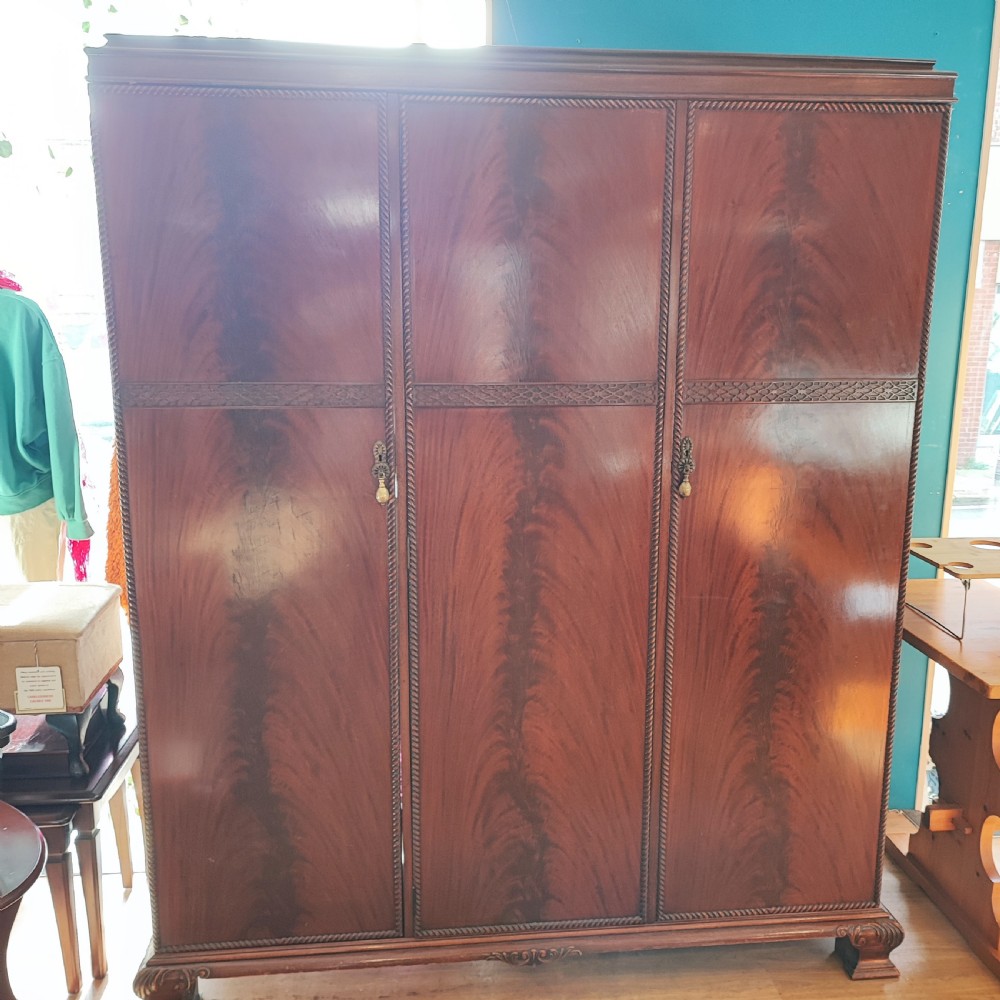 An Edwardian flame mahogany three-door wardrobe featuring carved rope twist moulding and carved bracket feet.