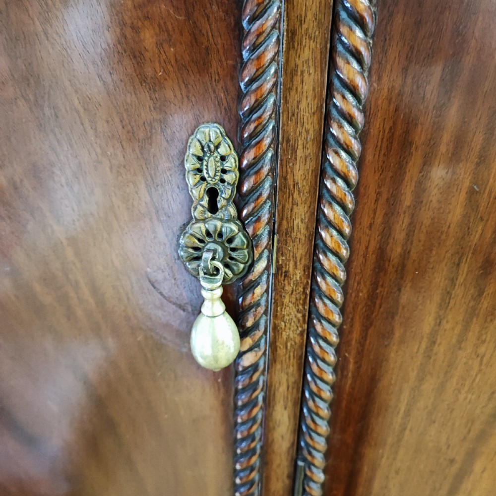 An Edwardian flame mahogany three-door wardrobe featuring carved rope twist moulding and carved bracket feet. View IV