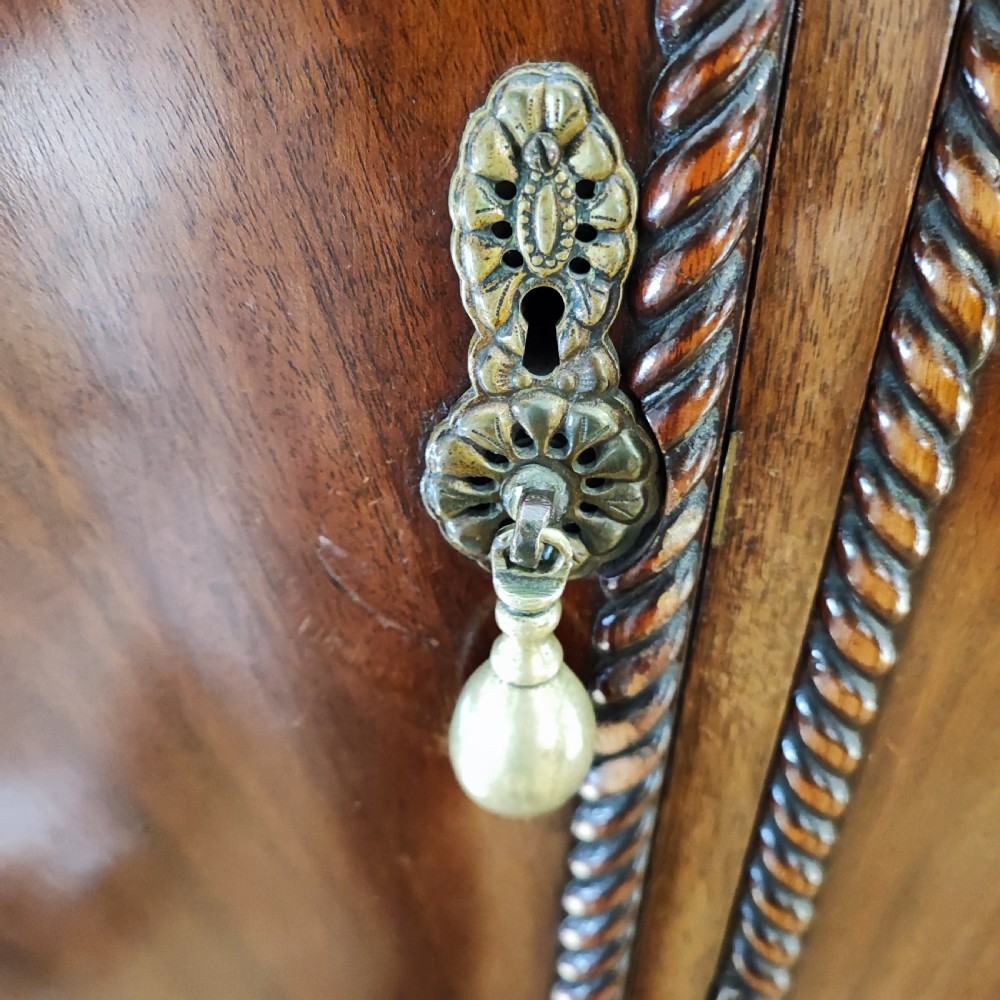 An Edwardian flame mahogany three-door wardrobe featuring carved rope twist moulding and carved bracket feet. View VI