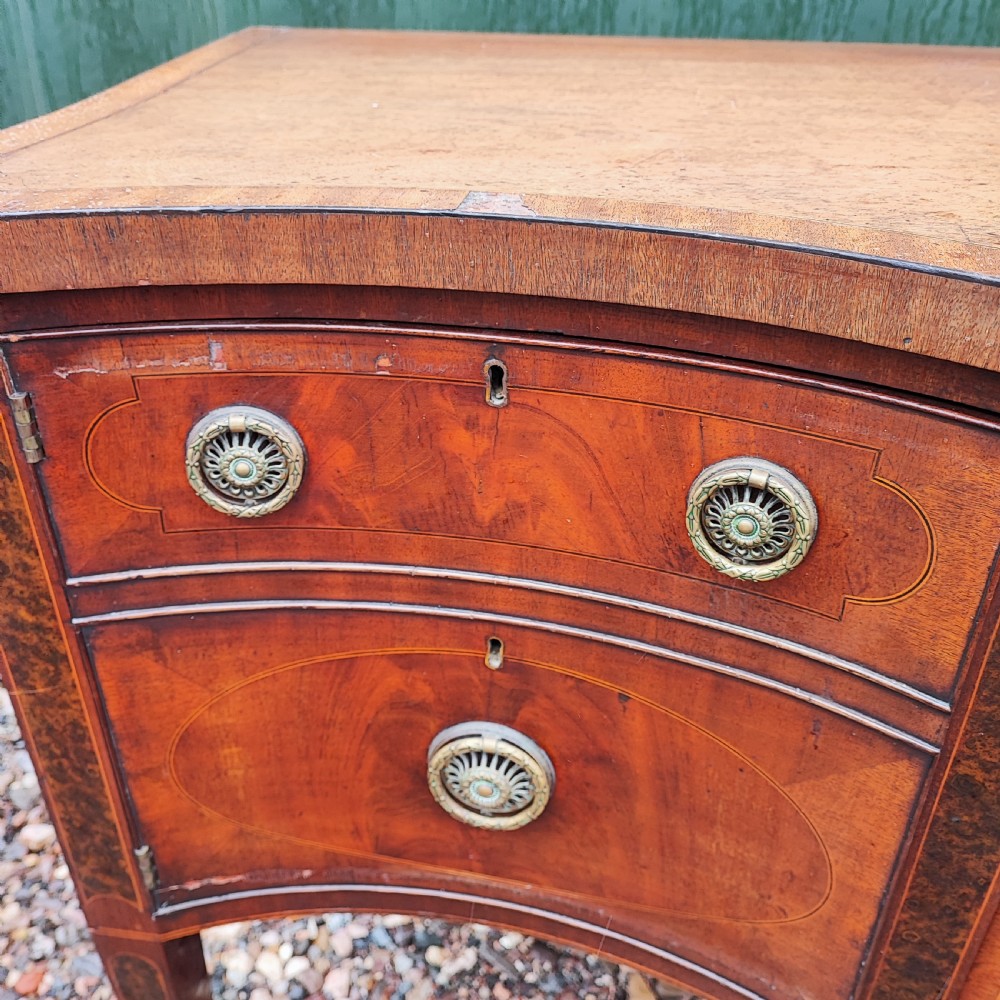 A George III style serpentine mahogany sideboard featuring marquetry inlay, brass ring handles, an arched central drawer, and square tapered legs. View III