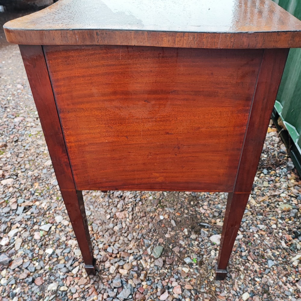 A George III style serpentine mahogany sideboard featuring marquetry inlay, brass ring handles, an arched central drawer, and square tapered legs. View IV