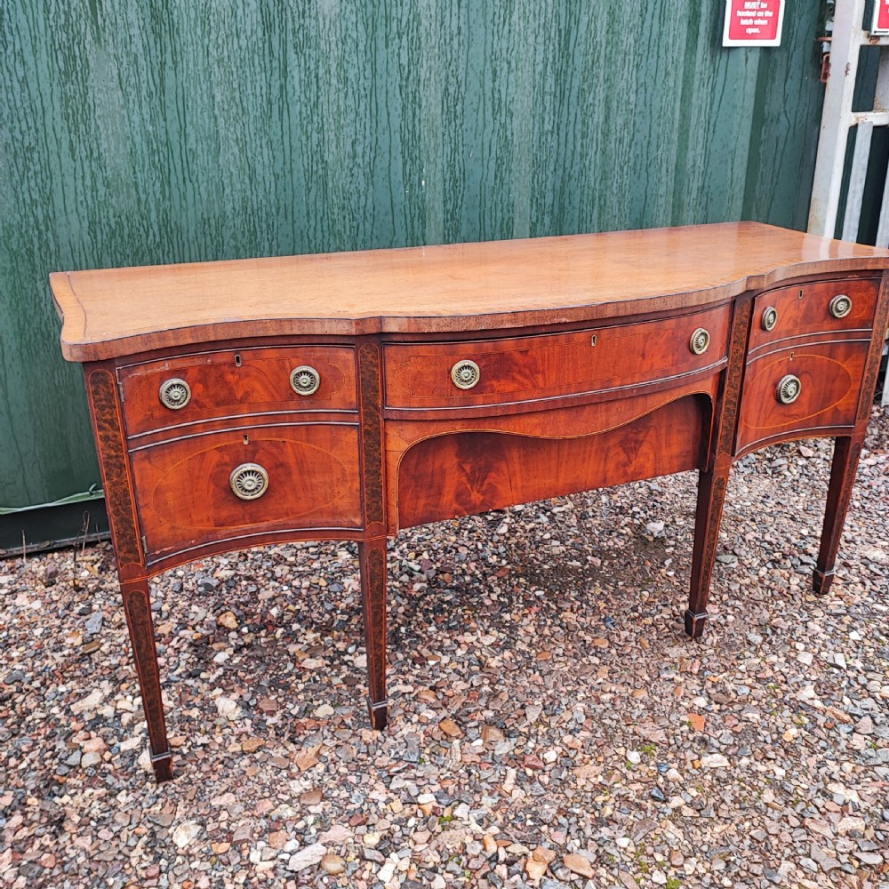 A George III style serpentine mahogany sideboard featuring marquetry inlay, brass ring handles, an arched central drawer, and square tapered legs. View IX