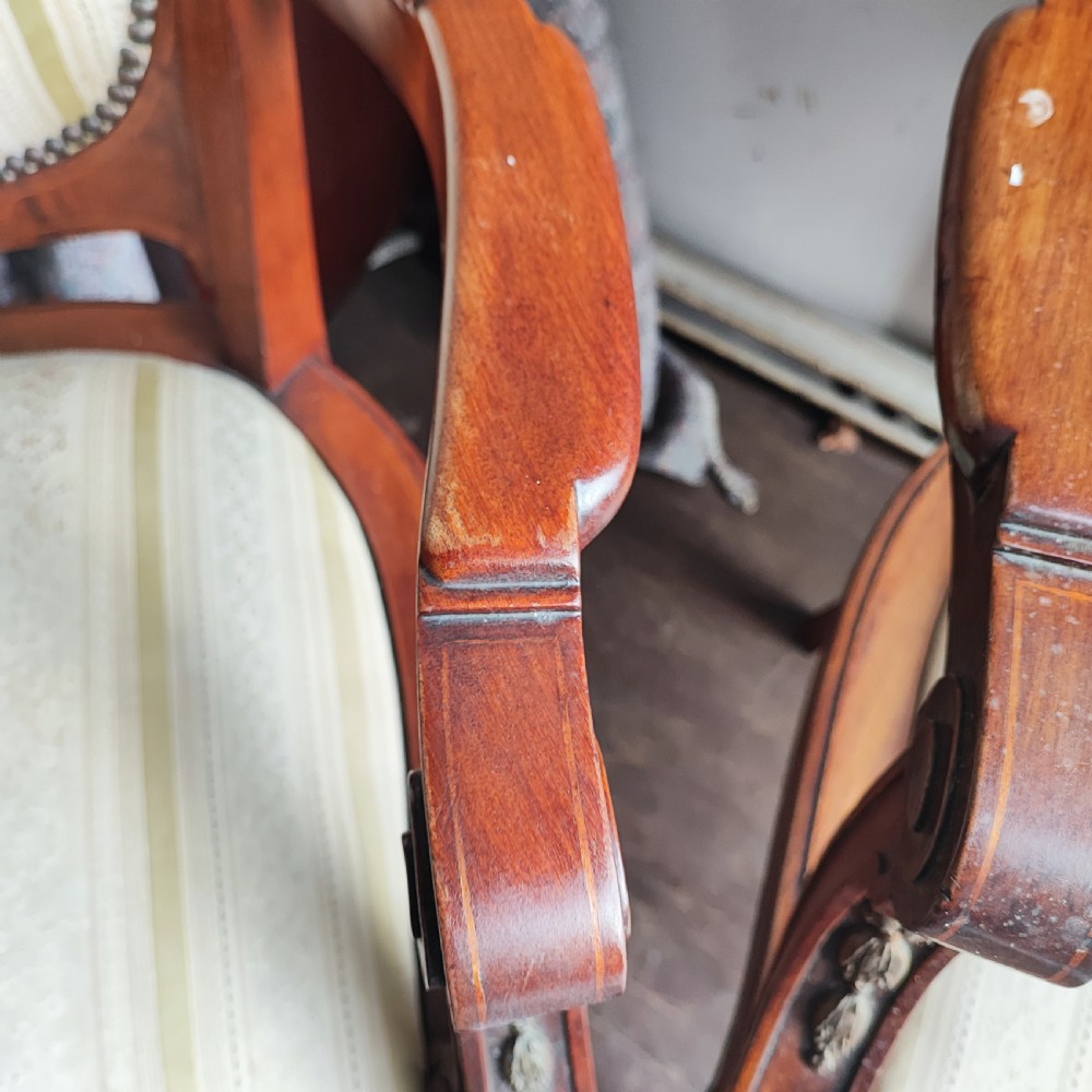 A pair of antique mahogany armchairs featuring cream and gold striped upholstery, curved cabriole legs, brass embellishments, and metal trim. View V