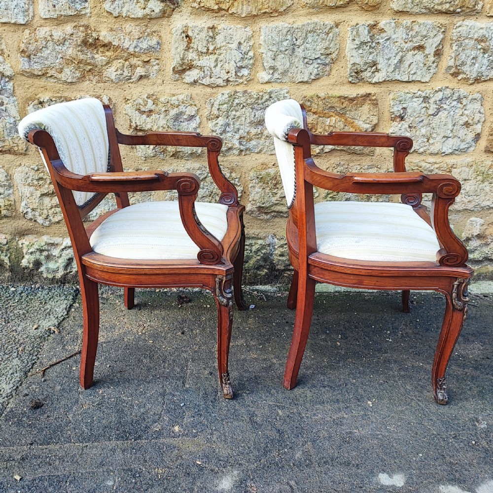A pair of antique mahogany armchairs featuring cream and gold striped upholstery, curved cabriole legs, brass embellishments, and metal trim. View VI