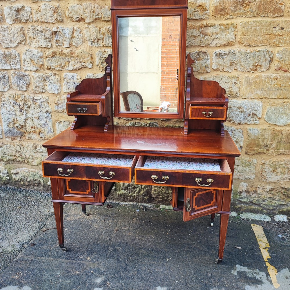 An Edwardian mahogany dressing table with satinwood inlay, an upright swinging central mirror, upper trinket drawers, and main drawers on tapering legs.