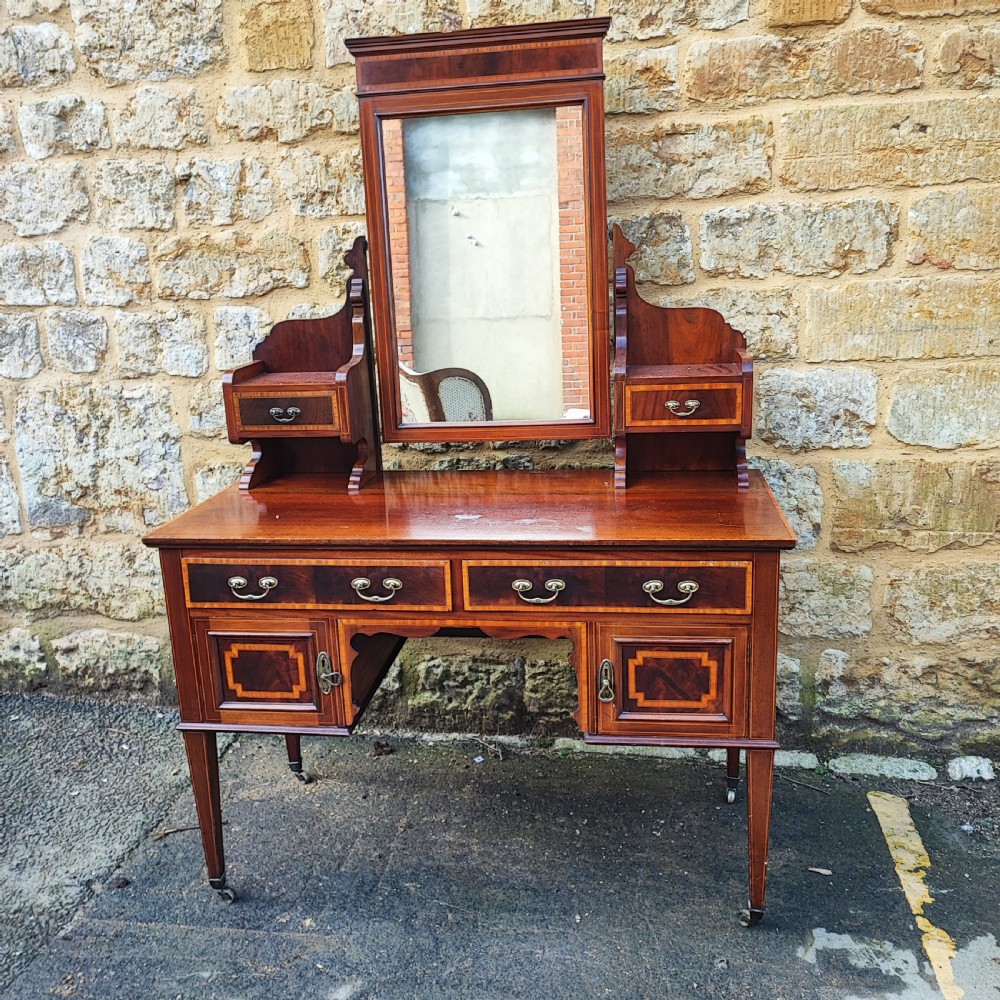 An Edwardian mahogany dressing table with satinwood inlay, an upright swinging central mirror, upper trinket drawers, and main drawers on tapering legs. View II