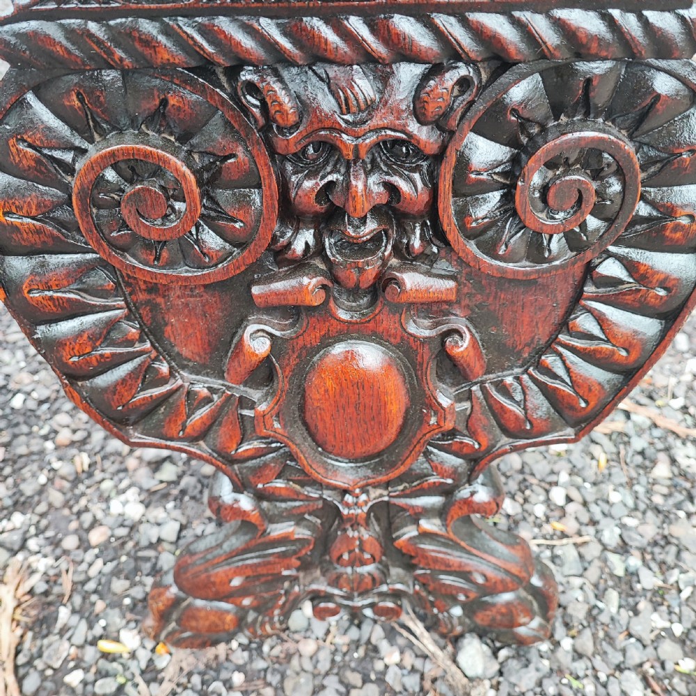 A pair of dark oak sgabello hall chairs featuring heavily carved fan-shaped backrests with figural details, octagonal seats, and ornate trestle bases. View IV