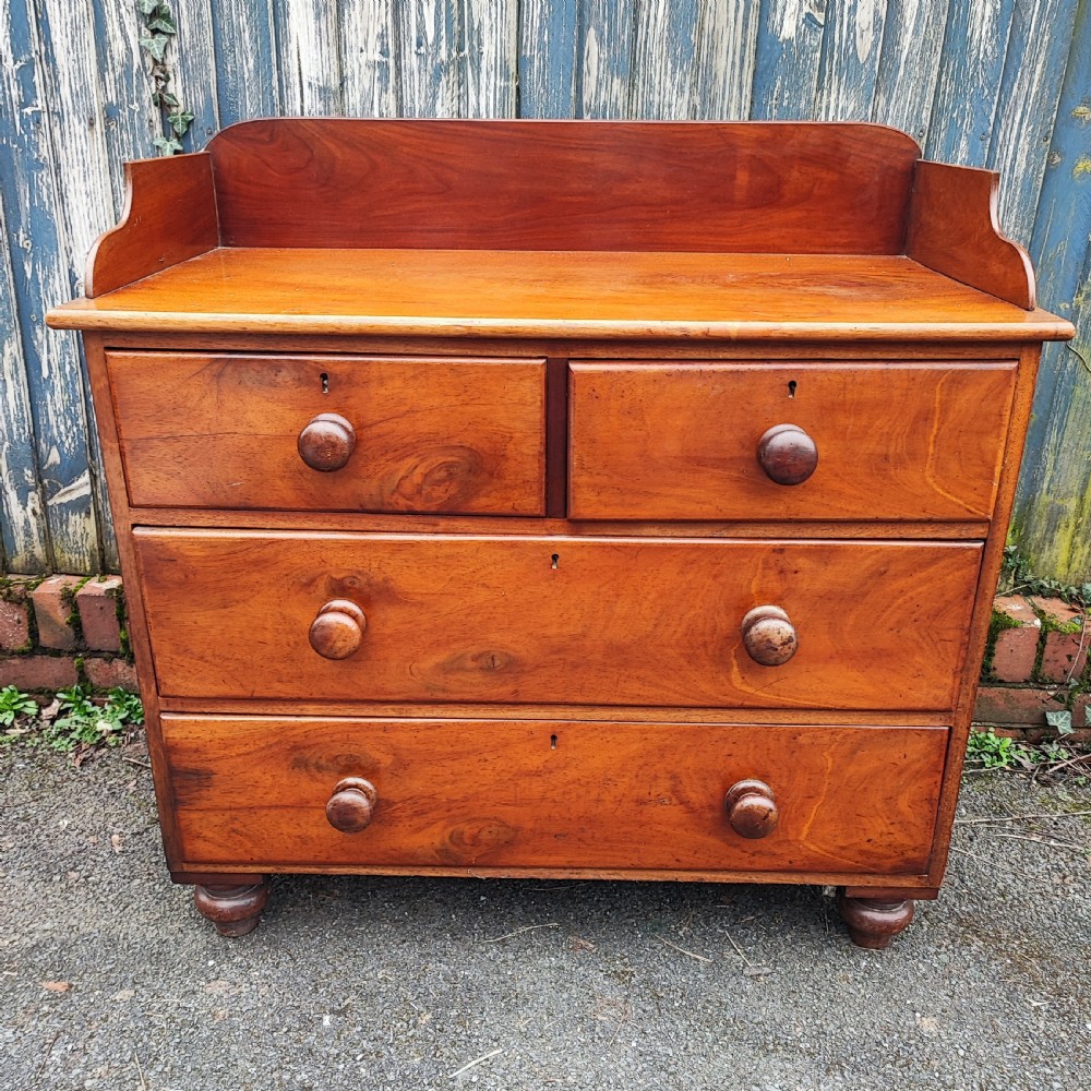 A small Victorian mahogany chest of drawers featuring a rear gallery upstand, two short over two long drawers, and round turned wooden handles. View V