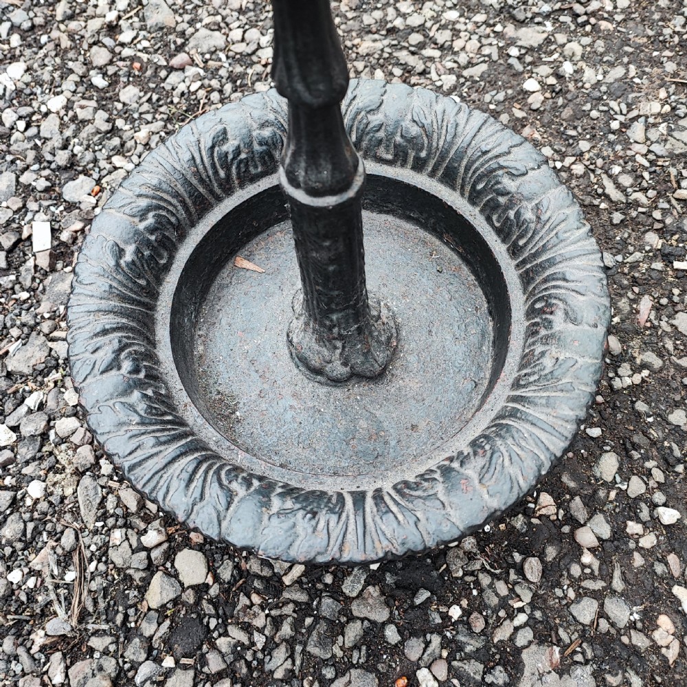 A Victorian black cast iron stick stand with an acorn finial, a four-section umbrella divider, and a circular leaf-embossed drip tray. View III