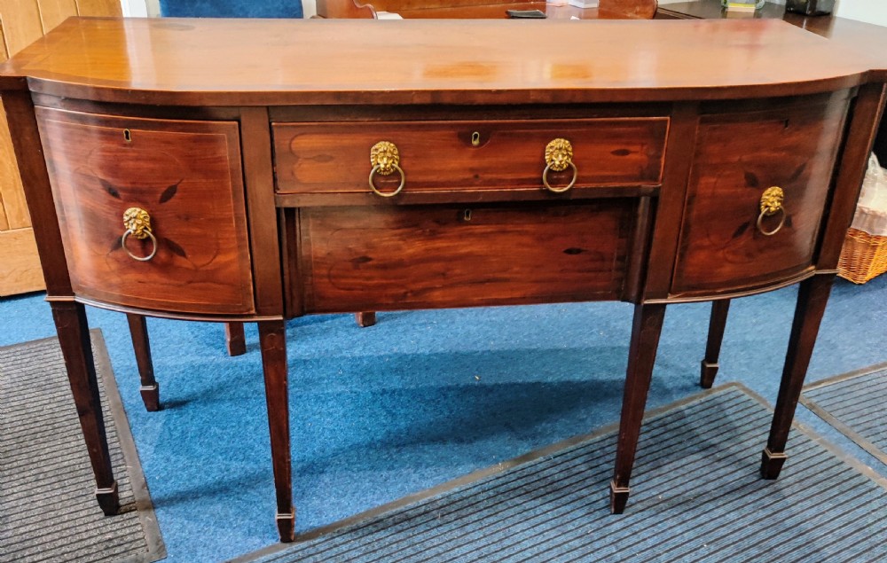 A Regency mahogany bowfront sideboard featuring inlaid floral motifs, brass lion-mask ring handles, and tapered square legs.