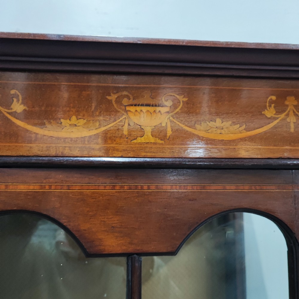 An Edwardian mahogany display cabinet featuring satinwood inlay, glazed doors with central floral motifs, and shaped legs. View V