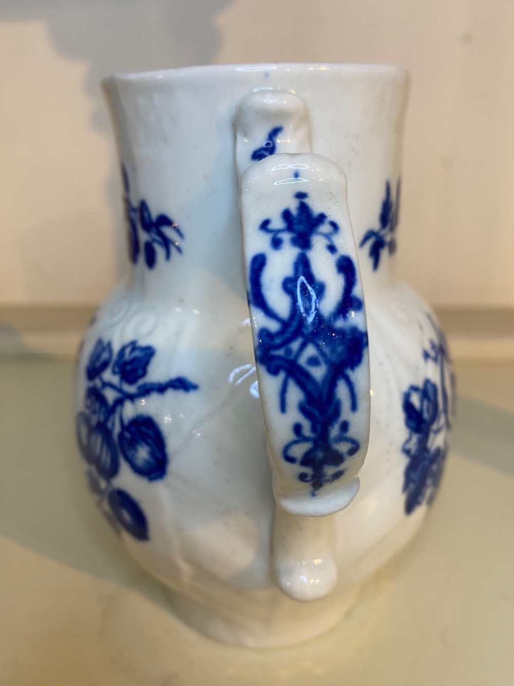 An antique Worcester blue and white porcelain jug featuring a moulded cabbage-leaf pattern, a bearded face mask spout, and bird decoration. View V