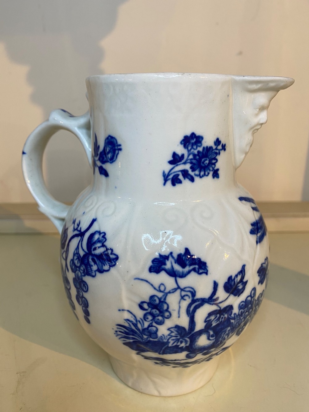 An antique Worcester blue and white porcelain jug featuring a moulded cabbage-leaf pattern, a bearded face mask spout, and bird decoration. View VI