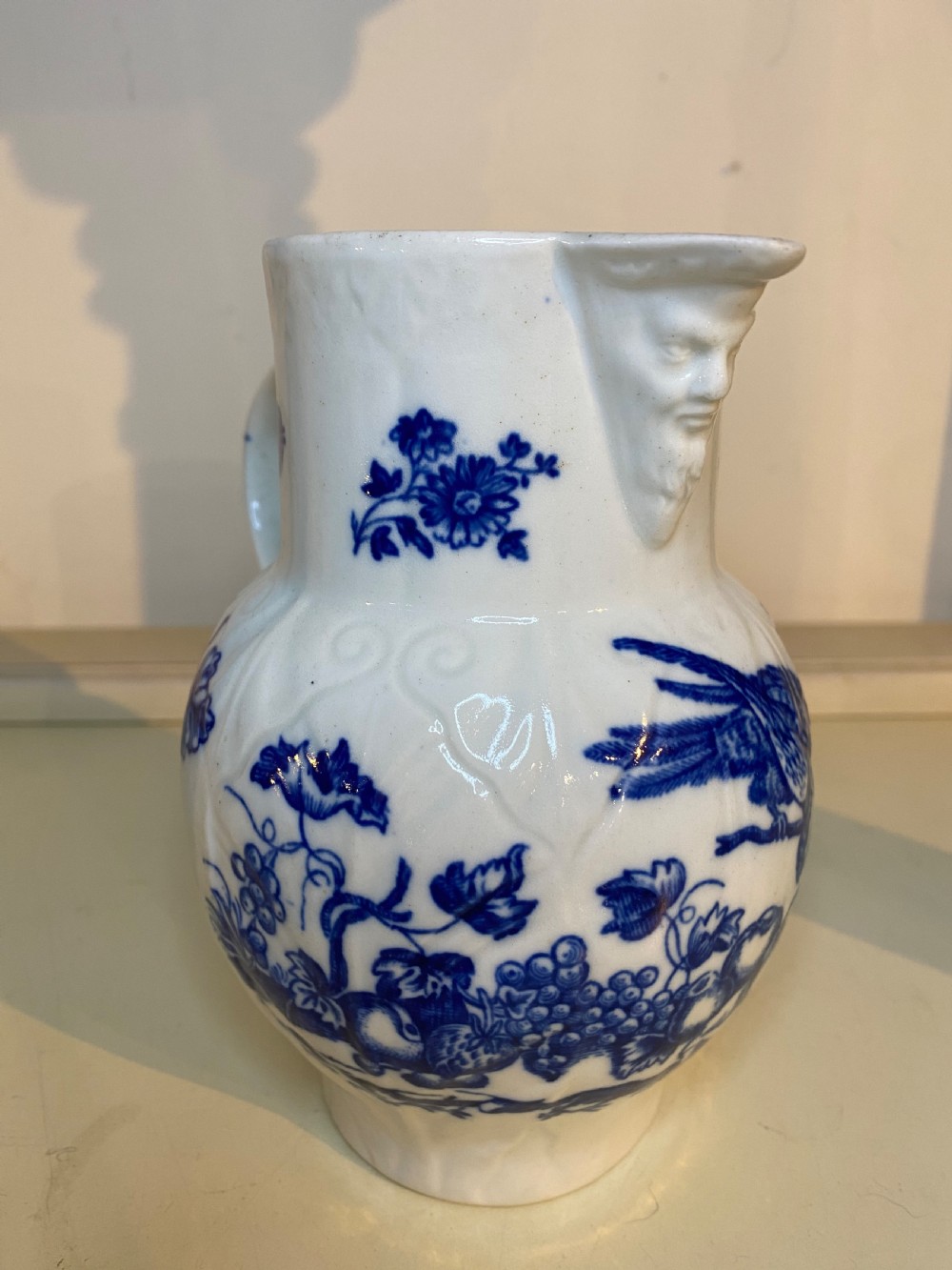 An antique Worcester blue and white porcelain jug featuring a moulded cabbage-leaf pattern, a bearded face mask spout, and bird decoration. View IX