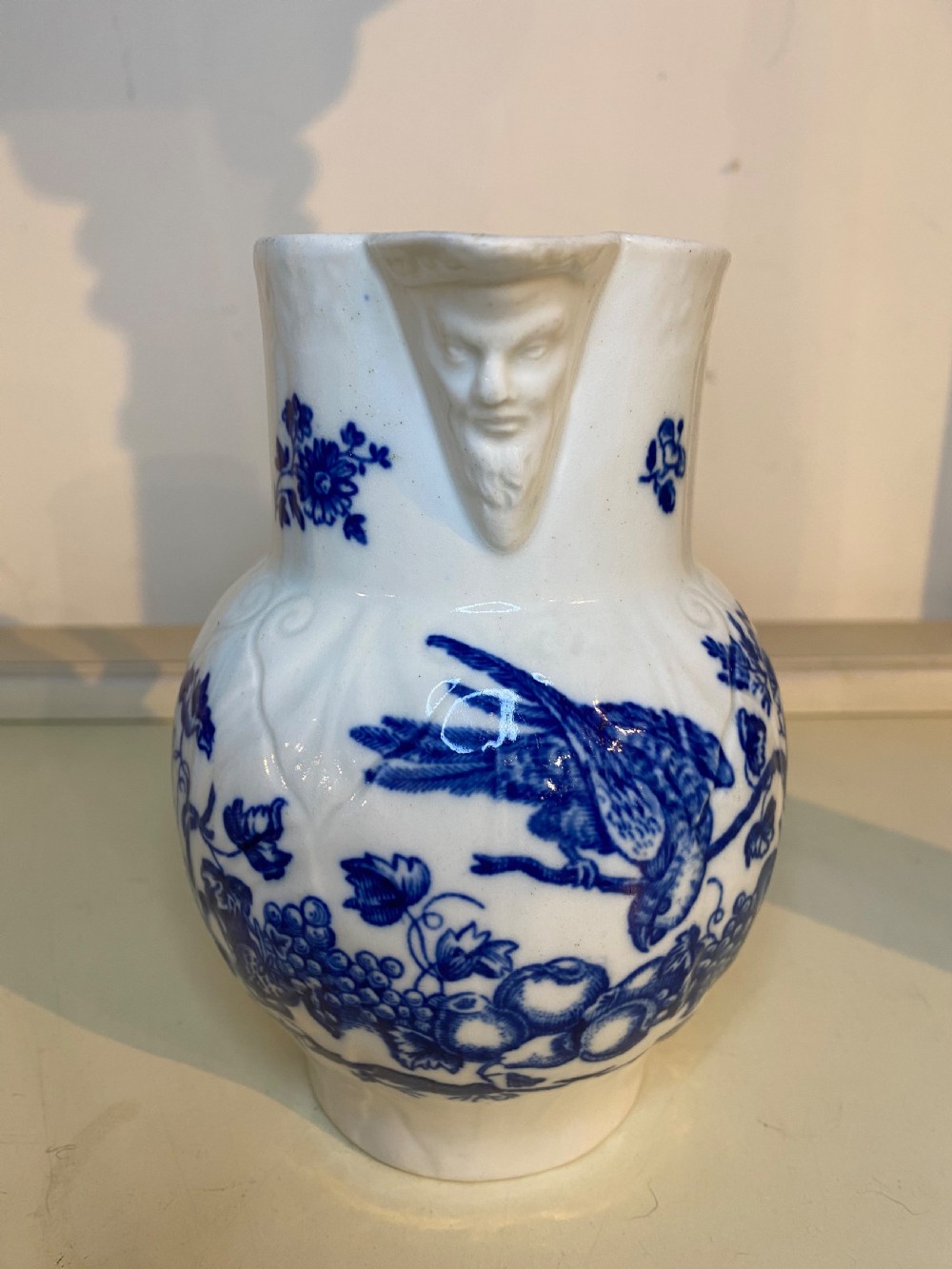 An antique Worcester blue and white porcelain jug featuring a moulded cabbage-leaf pattern, a bearded face mask spout, and bird decoration. View X