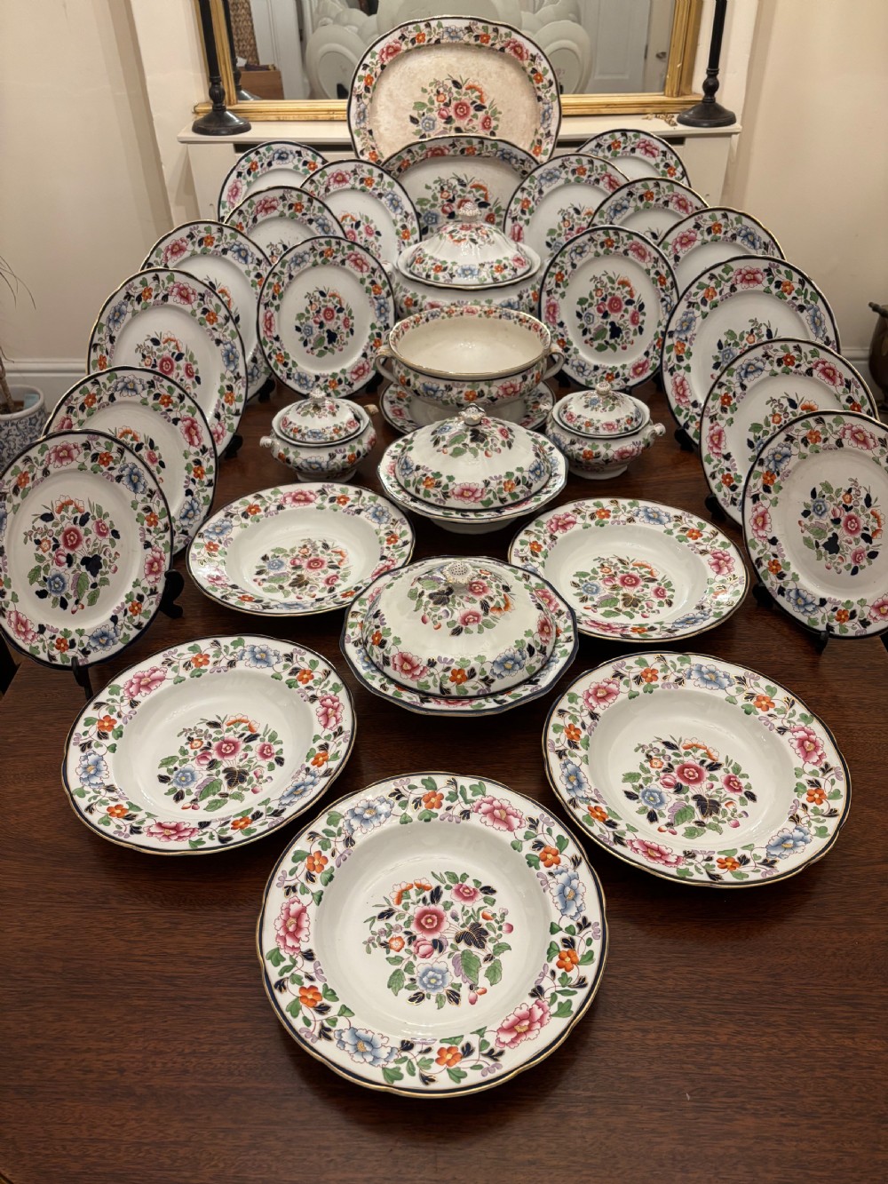 An extensive antique ceramic dinner service featuring floral transfers, matching tureens, bowls, and serving platters arranged together.