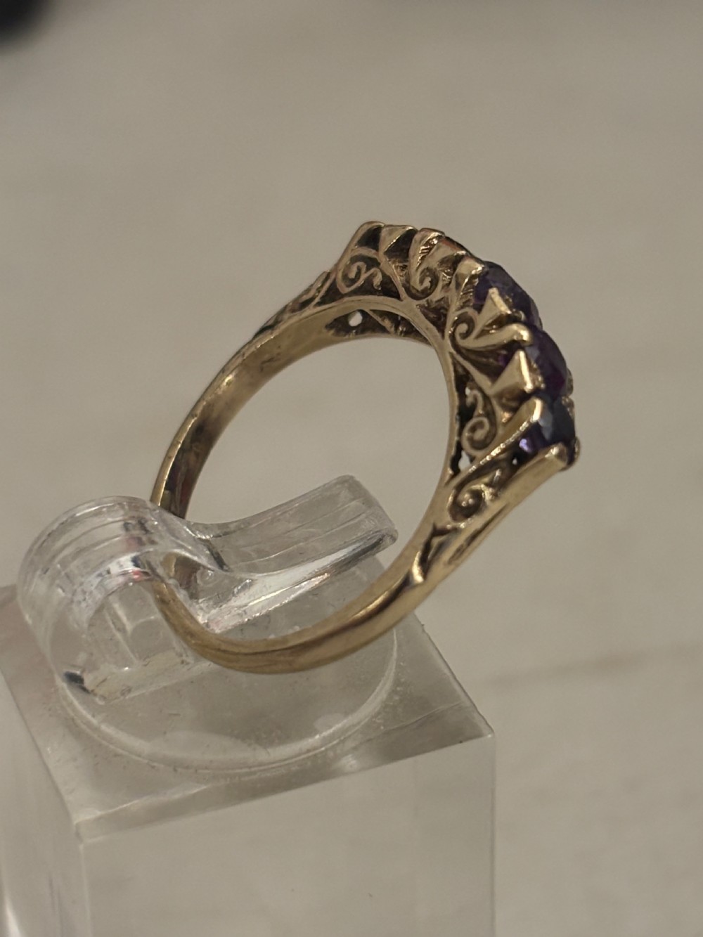 A yellow gold five stone ring set with five graduated round purple amethyst gemstones and carved scrollwork on the side gallery. View III