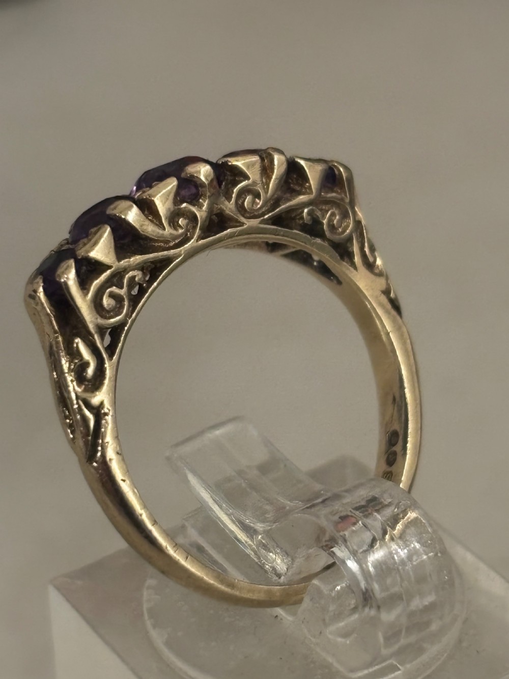A yellow gold five stone ring set with five graduated round purple amethyst gemstones and carved scrollwork on the side gallery. View IV