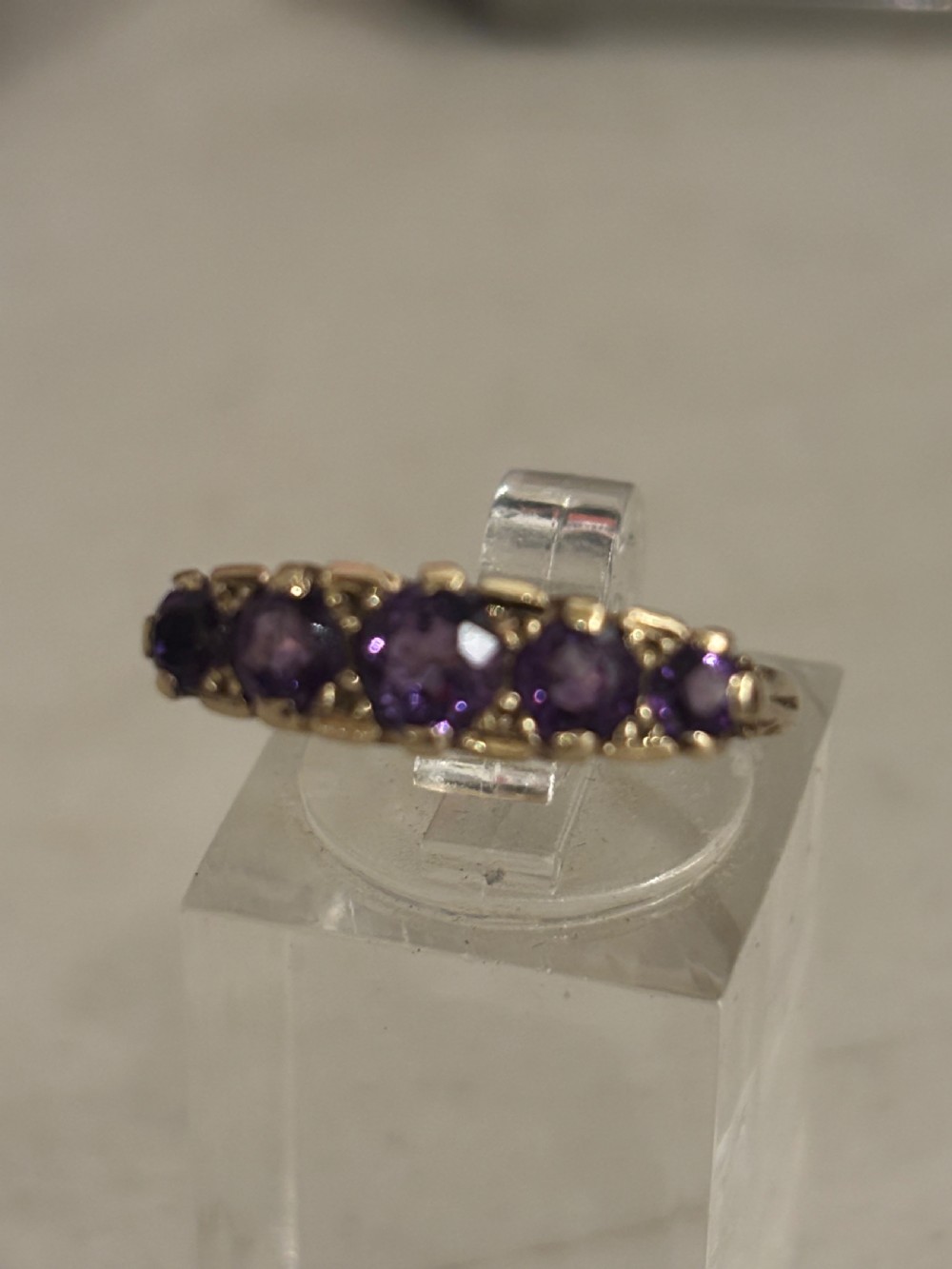 A yellow gold five stone ring set with five graduated round purple amethyst gemstones and carved scrollwork on the side gallery. View VIII