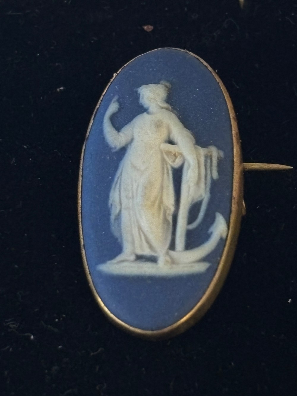 An oval blue jasperware brooch featuring a white bas-relief classical female figure with an anchor, mounted in a metal frame. View III