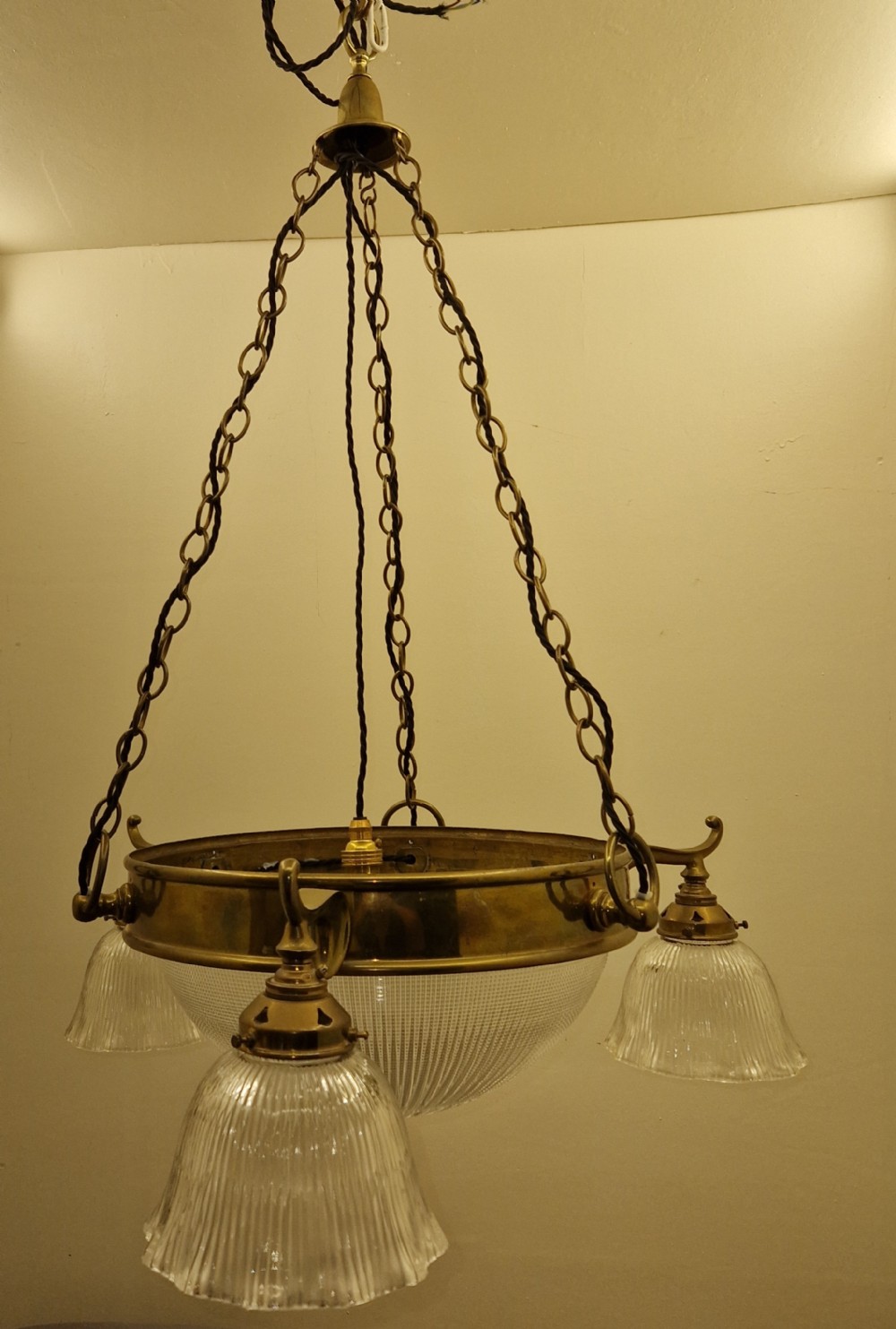 An Edwardian brass ceiling light fitting featuring three chain-suspended stiletto glass shades surrounding a central prismatic glass bowl.