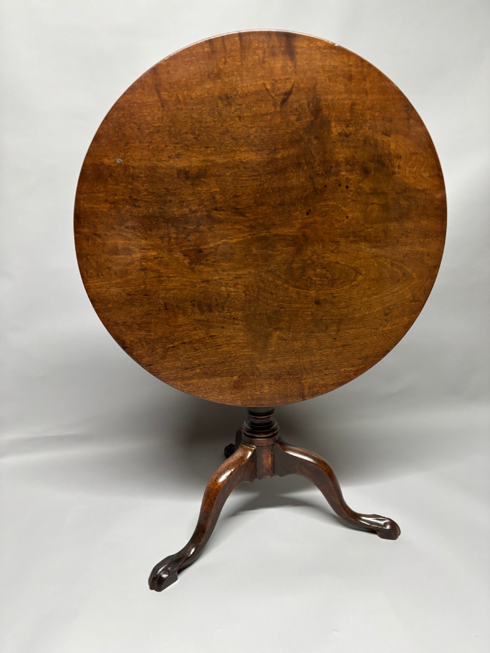 A solid circular mahogany tilt-top table shown tilted vertically on a central turned column with three cabriole legs.