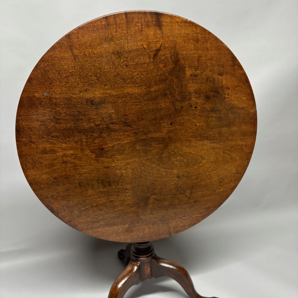 A solid circular mahogany tilt-top table shown tilted vertically on a central turned column with three cabriole legs. View II