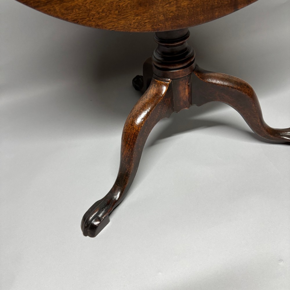 A solid circular mahogany tilt-top table shown tilted vertically on a central turned column with three cabriole legs. View III