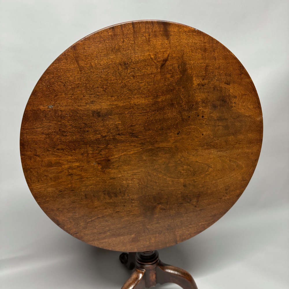 A solid circular mahogany tilt-top table shown tilted vertically on a central turned column with three cabriole legs. View IV