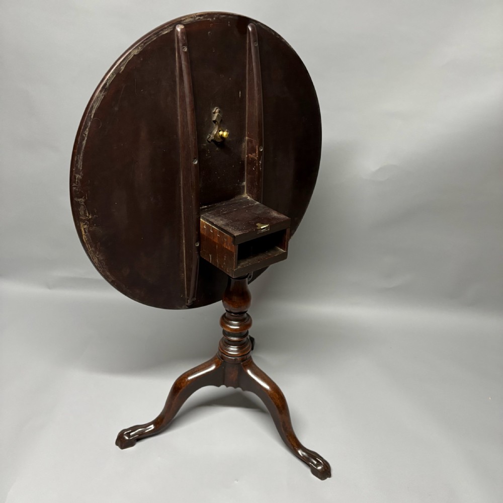 A solid circular mahogany tilt-top table shown tilted vertically on a central turned column with three cabriole legs. View V