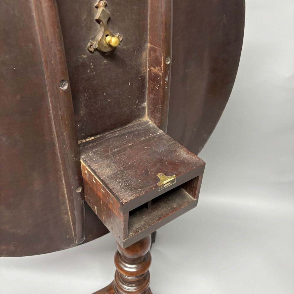 A solid circular mahogany tilt-top table shown tilted vertically on a central turned column with three cabriole legs. View VI