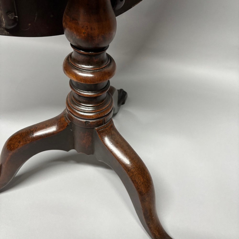 A solid circular mahogany tilt-top table shown tilted vertically on a central turned column with three cabriole legs. View IX