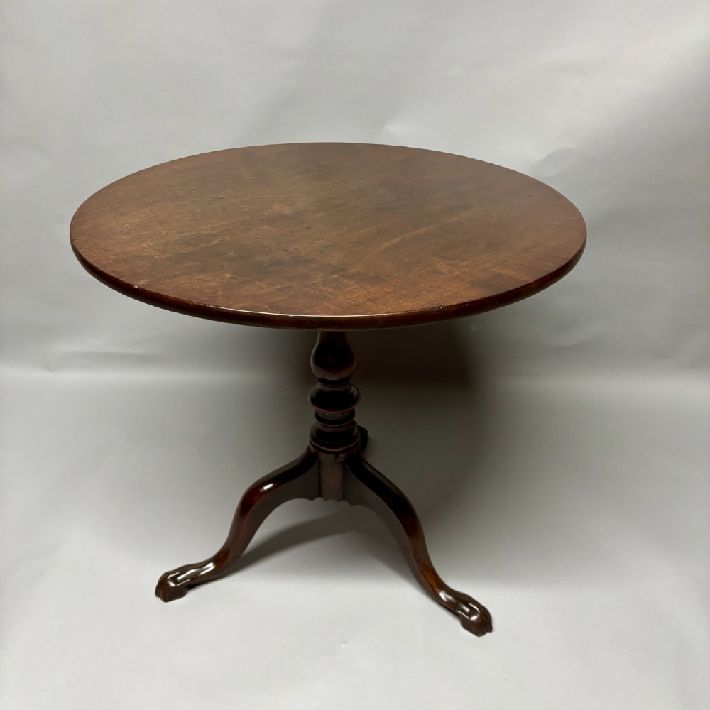 A solid circular mahogany tilt-top table shown tilted vertically on a central turned column with three cabriole legs. View X
