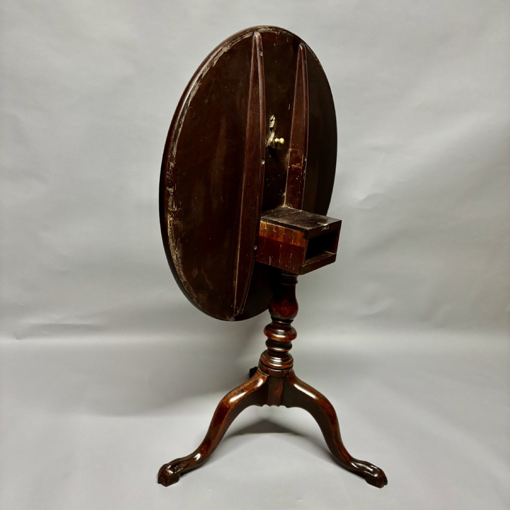 A solid circular mahogany tilt-top table shown tilted vertically on a central turned column with three cabriole legs. View XIII