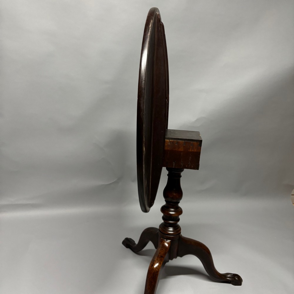 A solid circular mahogany tilt-top table shown tilted vertically on a central turned column with three cabriole legs. View XIV