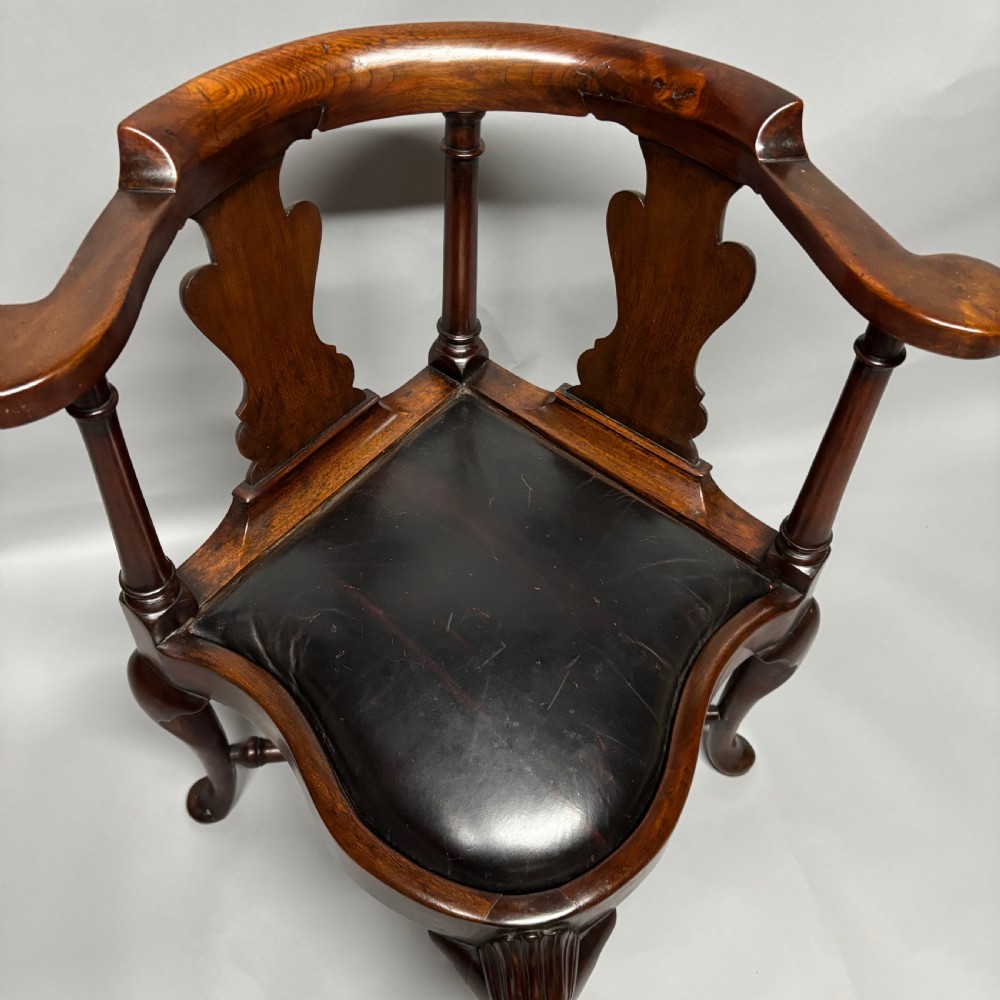An 18th-century George III dark mahogany corner chair featuring a curved top rail, twin shaped splats, a dark leather seat, turned stretchers, and a front cabriole leg carved with a shell motif. View III