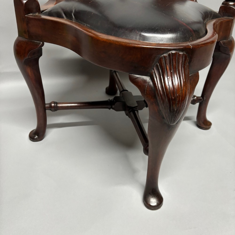 An 18th-century George III dark mahogany corner chair featuring a curved top rail, twin shaped splats, a dark leather seat, turned stretchers, and a front cabriole leg carved with a shell motif. View IV