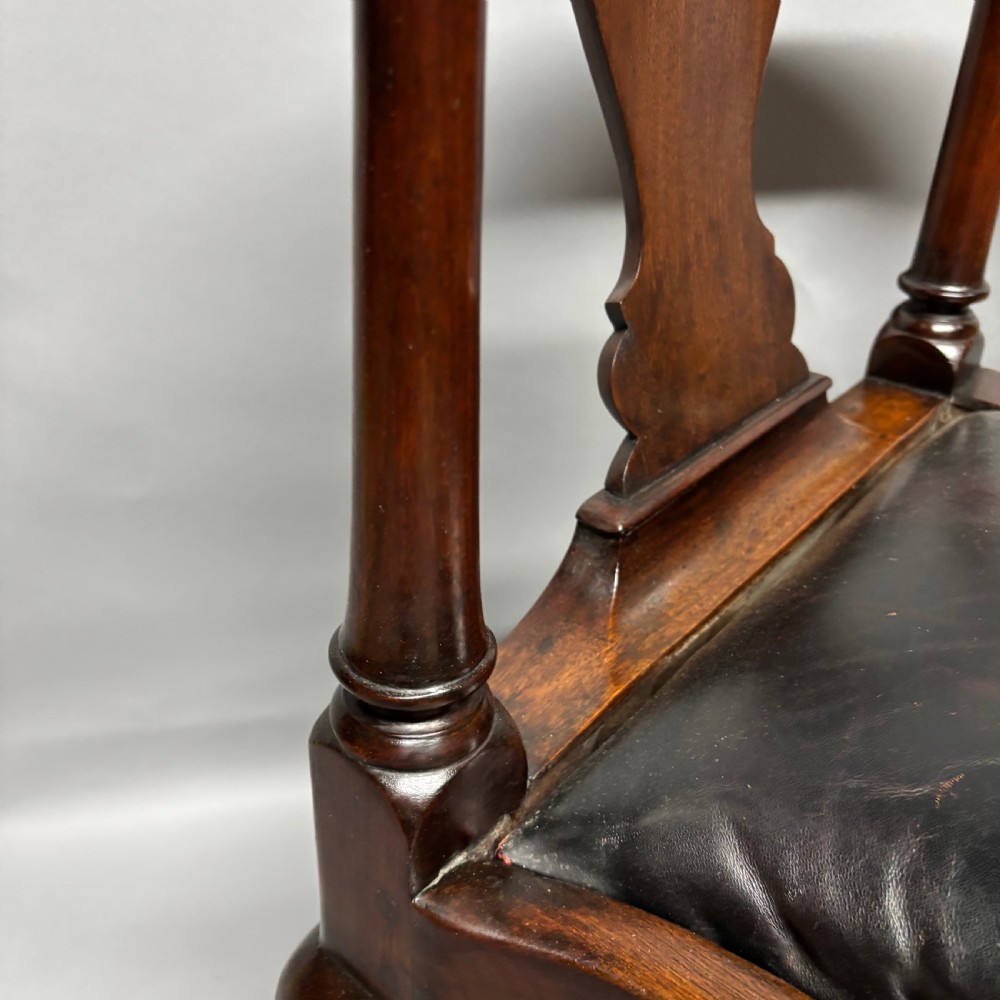 An 18th-century George III dark mahogany corner chair featuring a curved top rail, twin shaped splats, a dark leather seat, turned stretchers, and a front cabriole leg carved with a shell motif. View VII