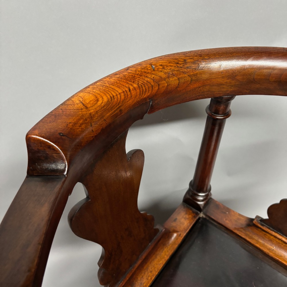 An 18th-century George III dark mahogany corner chair featuring a curved top rail, twin shaped splats, a dark leather seat, turned stretchers, and a front cabriole leg carved with a shell motif. View VIII