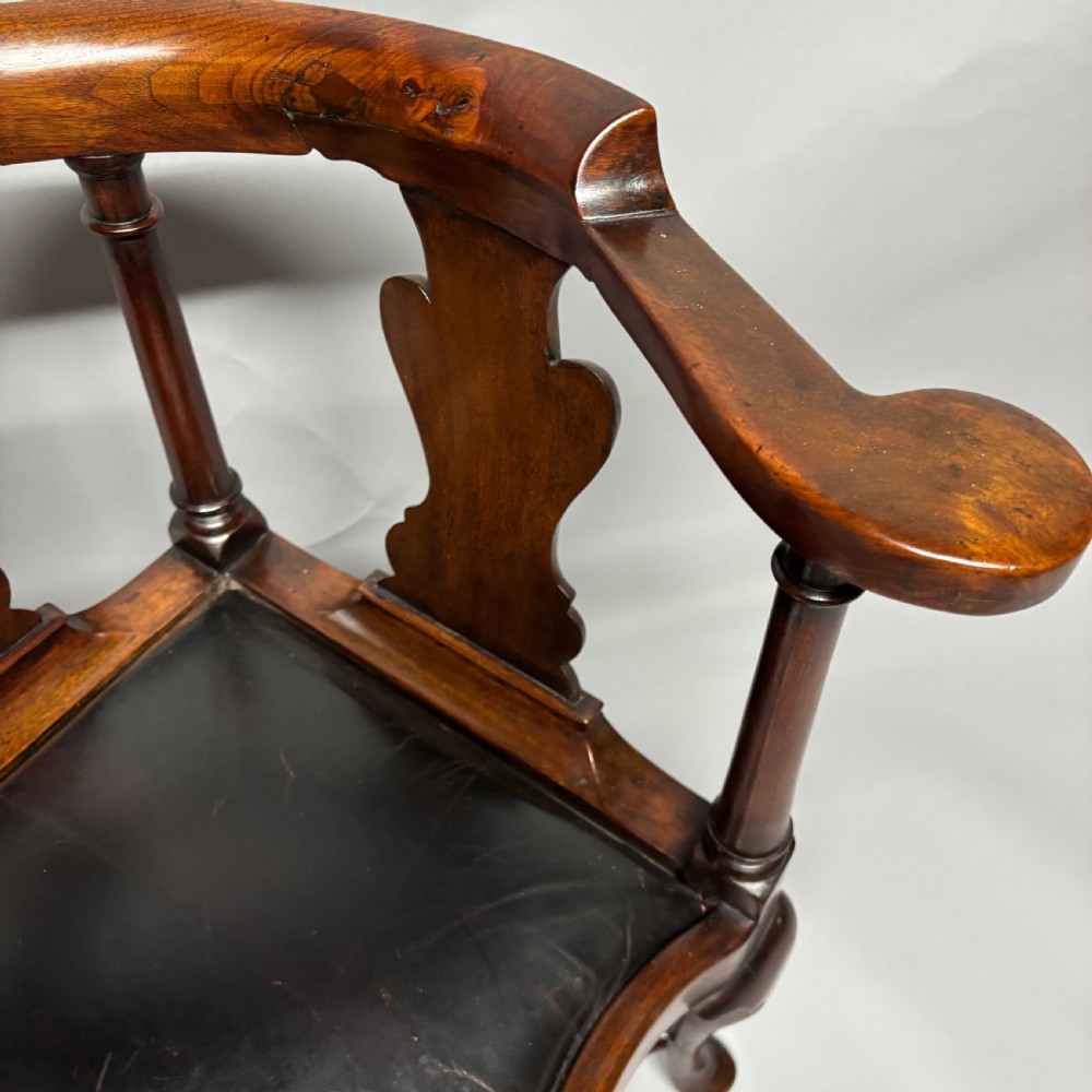 An 18th-century George III dark mahogany corner chair featuring a curved top rail, twin shaped splats, a dark leather seat, turned stretchers, and a front cabriole leg carved with a shell motif. View X